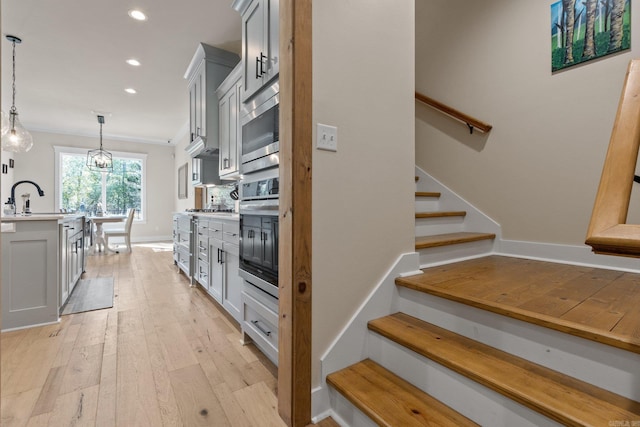 kitchen featuring light wood-type flooring, sink, stainless steel appliances, hanging light fixtures, and white cabinets