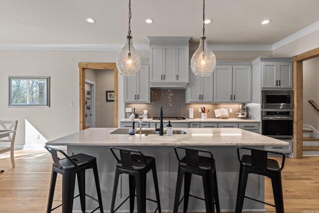 kitchen with light hardwood / wood-style floors, a center island with sink, stainless steel appliances, light stone countertops, and ornamental molding