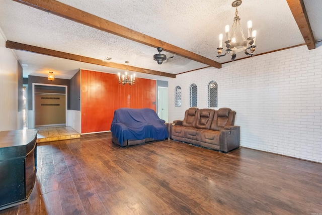 unfurnished living room featuring beamed ceiling, dark wood-type flooring, brick wall, and a textured ceiling