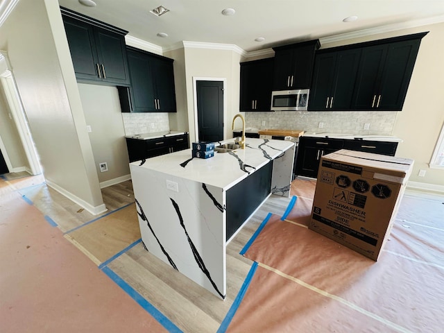 kitchen featuring tasteful backsplash, sink, crown molding, light hardwood / wood-style flooring, and an island with sink