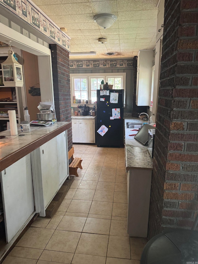 kitchen featuring light tile patterned flooring, sink, brick wall, and white cabinets