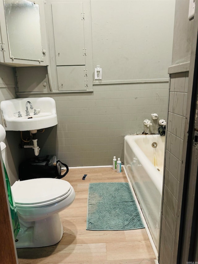 bathroom featuring sink, a washtub, hardwood / wood-style flooring, tile walls, and toilet