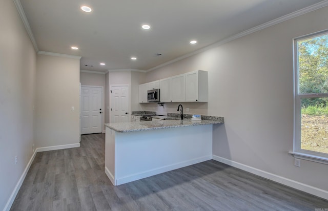 kitchen featuring light wood-type flooring, light stone counters, kitchen peninsula, appliances with stainless steel finishes, and white cabinetry