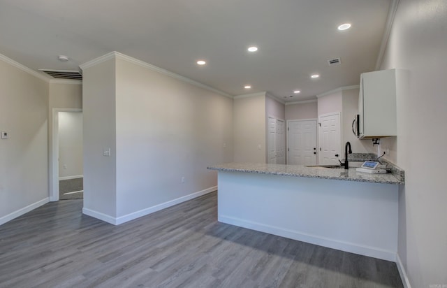 kitchen featuring light stone countertops, white cabinets, kitchen peninsula, crown molding, and light hardwood / wood-style flooring