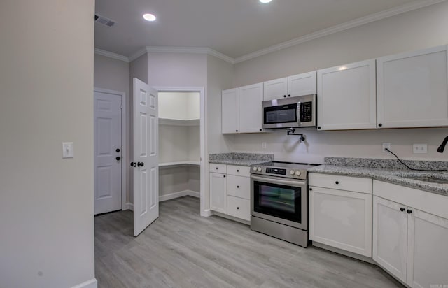 kitchen with light wood-type flooring, light stone countertops, stainless steel appliances, white cabinetry, and ornamental molding