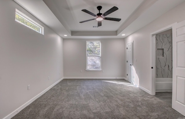 carpeted spare room featuring ceiling fan, a tray ceiling, and a wealth of natural light