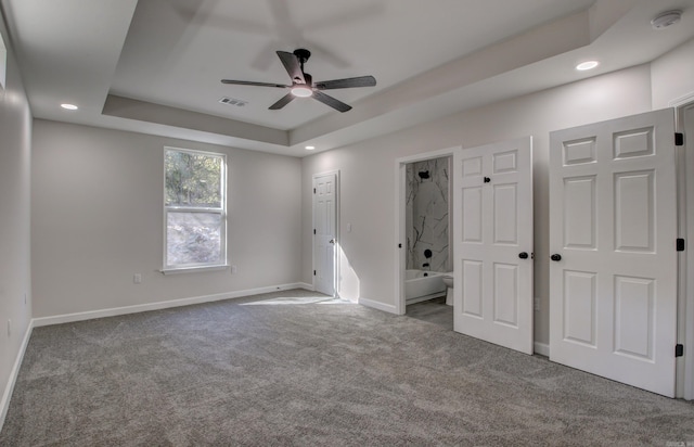 unfurnished bedroom featuring ensuite bathroom, carpet flooring, ceiling fan, and a raised ceiling