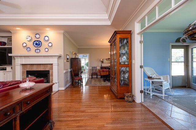 living room with light wood-type flooring, crown molding, and a tile fireplace