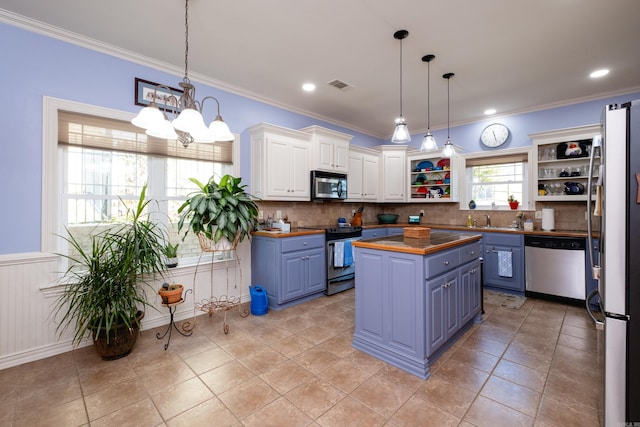 kitchen featuring a kitchen island, butcher block counters, stainless steel appliances, hanging light fixtures, and white cabinetry