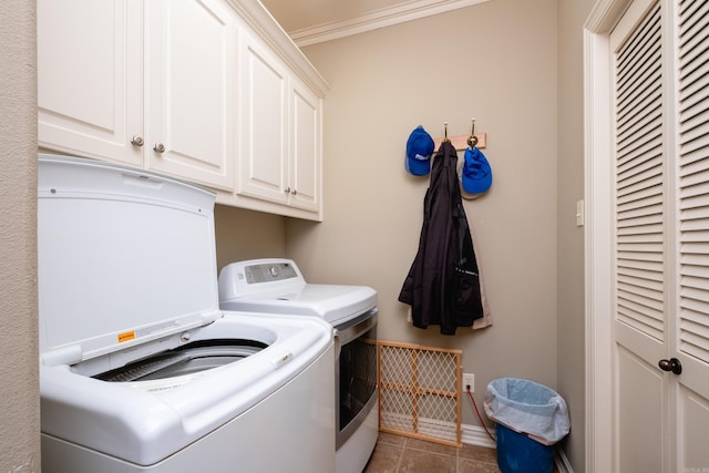 clothes washing area with washing machine and dryer, dark tile patterned floors, ornamental molding, and cabinets