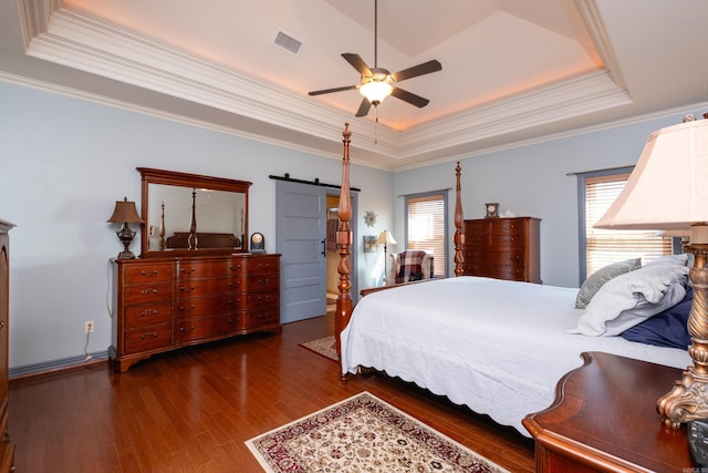 bedroom with ceiling fan, dark hardwood / wood-style floors, crown molding, a tray ceiling, and a barn door