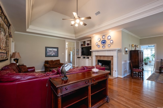 living room featuring ceiling fan, lofted ceiling, a tiled fireplace, hardwood / wood-style flooring, and crown molding