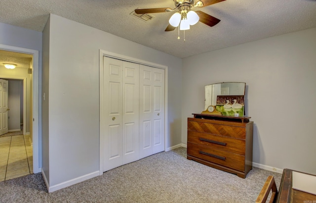 bedroom featuring a closet, light colored carpet, a textured ceiling, and ceiling fan