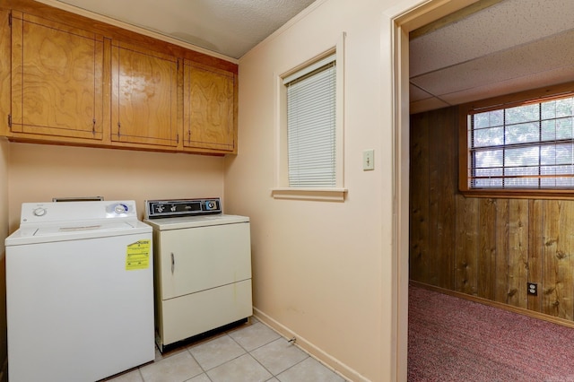 laundry area with wooden walls, washer and clothes dryer, light tile patterned flooring, cabinets, and a textured ceiling