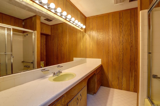 bathroom with wooden walls, tile patterned floors, a shower with shower door, and vanity