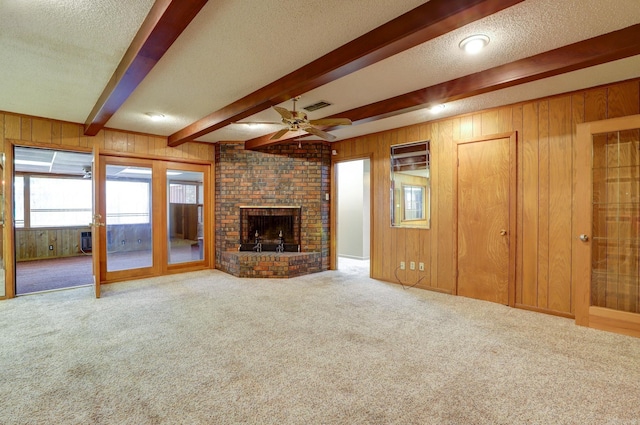 unfurnished living room with a brick fireplace, beam ceiling, wood walls, and carpet flooring