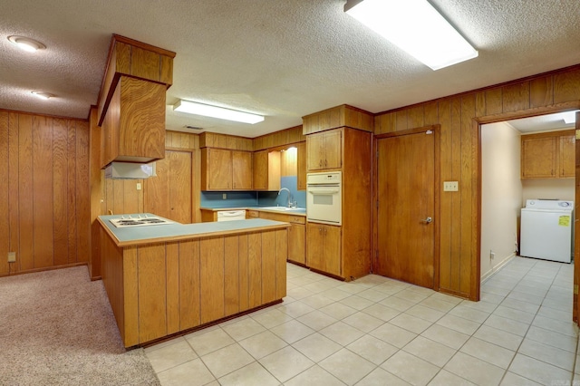 kitchen with wood walls, white appliances, sink, washer / dryer, and kitchen peninsula