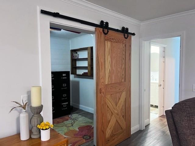 corridor with a barn door, ornamental molding, and dark hardwood / wood-style flooring