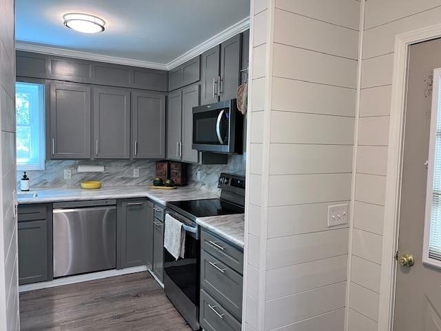 kitchen featuring gray cabinetry, crown molding, dark wood-type flooring, stainless steel appliances, and backsplash