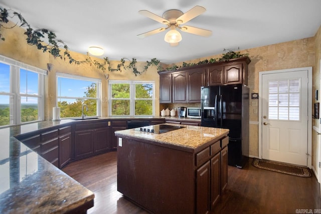 kitchen featuring sink, stone counters, black appliances, dark hardwood / wood-style floors, and a center island