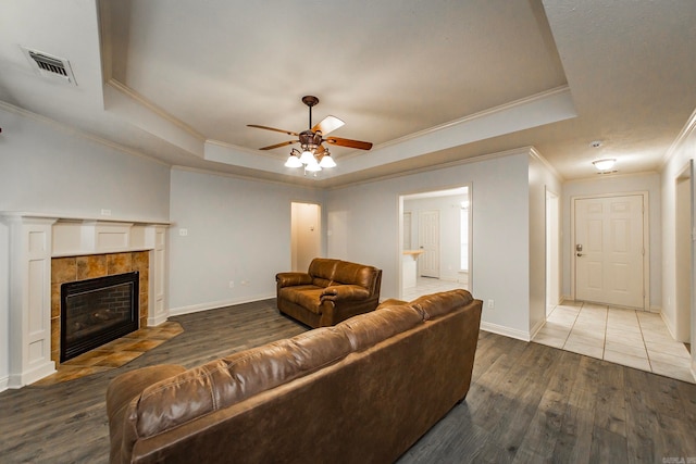 living room with wood-type flooring, crown molding, a tray ceiling, and a tile fireplace