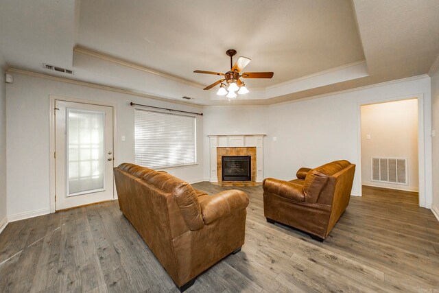 living room with wood-type flooring, a raised ceiling, crown molding, and a tiled fireplace