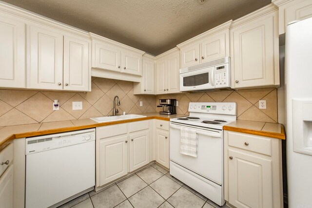 kitchen with decorative backsplash, white appliances, sink, light tile patterned floors, and a textured ceiling