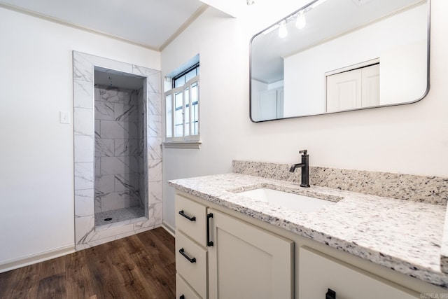 bathroom with crown molding, hardwood / wood-style floors, vanity, and tiled shower