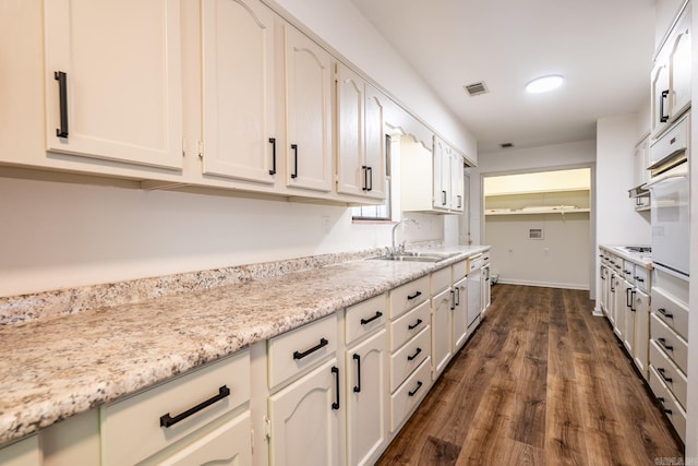 kitchen with light stone counters, white cabinets, sink, white appliances, and dark wood-type flooring