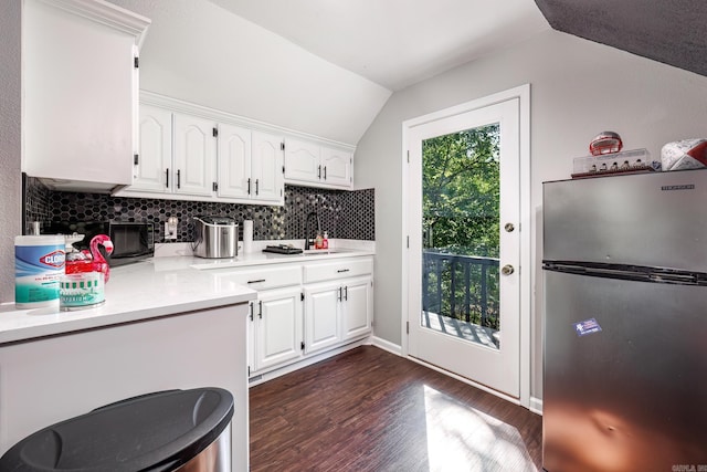 kitchen featuring tasteful backsplash, white cabinets, dark wood-type flooring, stainless steel refrigerator, and vaulted ceiling