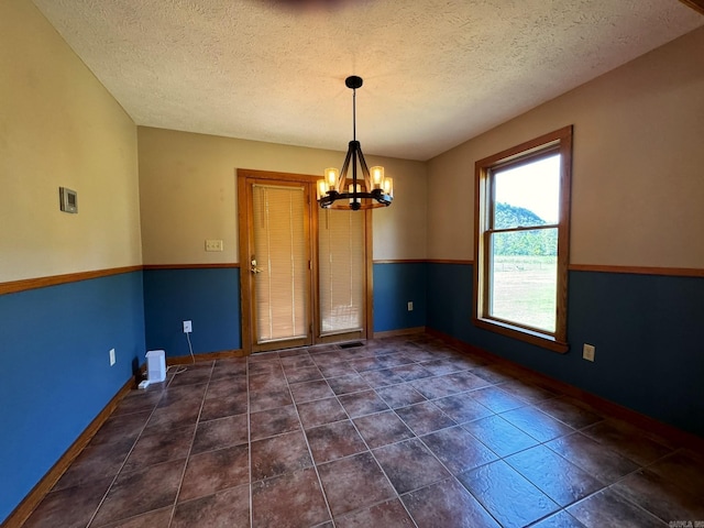 empty room with dark tile patterned flooring, baseboards, a notable chandelier, and a textured ceiling