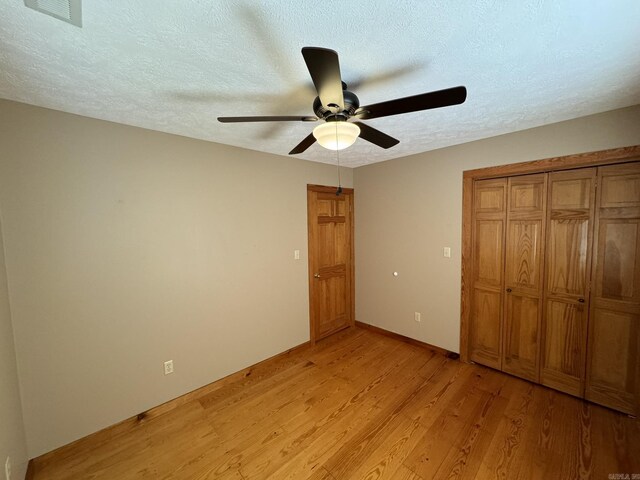 unfurnished bedroom with a closet, baseboards, a textured ceiling, light wood-style floors, and visible vents
