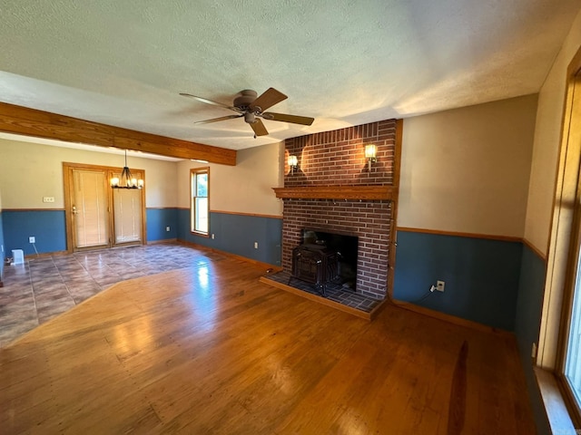 unfurnished living room featuring ceiling fan with notable chandelier, wainscoting, wood finished floors, and a textured ceiling