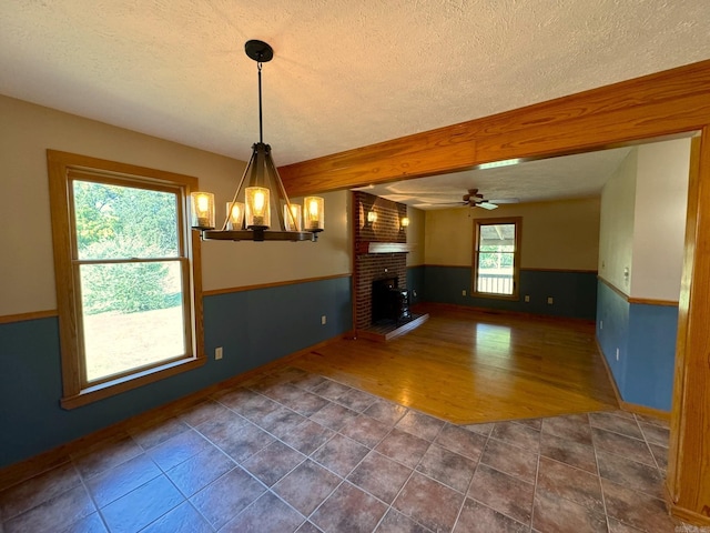 unfurnished dining area featuring ceiling fan, a fireplace, a textured ceiling, dark tile patterned floors, and wainscoting