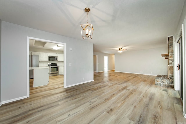 unfurnished living room featuring ceiling fan with notable chandelier and light hardwood / wood-style floors