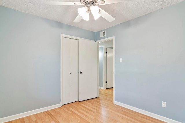 unfurnished bedroom featuring ceiling fan, a textured ceiling, light wood-type flooring, and a closet