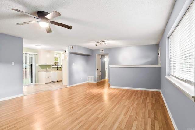 unfurnished living room featuring ceiling fan, sink, light hardwood / wood-style flooring, and a textured ceiling