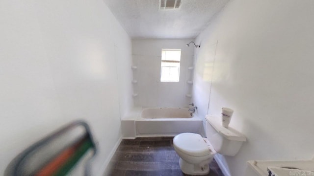 bathroom featuring a textured ceiling, toilet, and tiled shower / bath combo