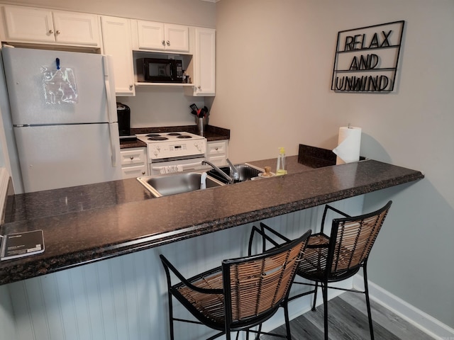 kitchen featuring white appliances, a kitchen bar, sink, and white cabinetry