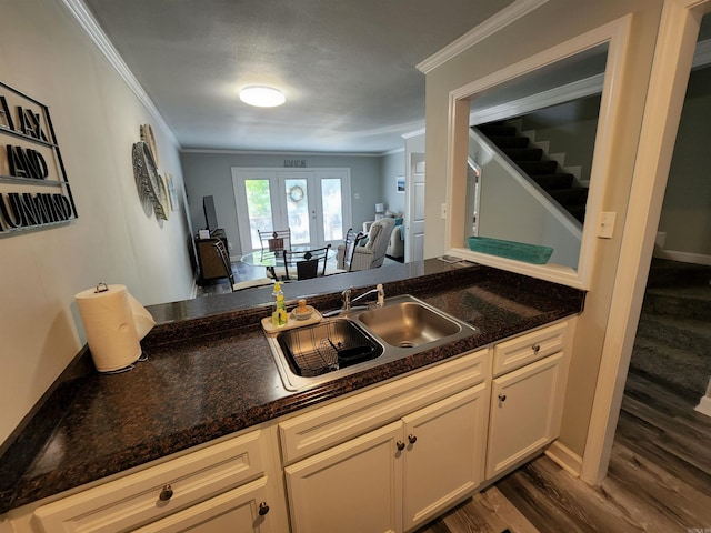 kitchen with dark wood-type flooring, sink, kitchen peninsula, dark stone counters, and crown molding