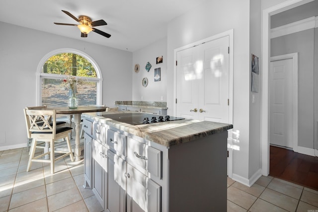 kitchen featuring black electric cooktop, ceiling fan, a center island, and light tile patterned floors