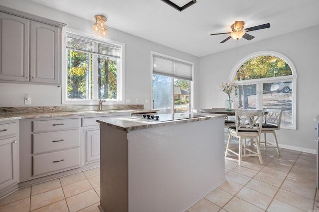 kitchen with light tile patterned flooring, black electric stovetop, a center island, and ceiling fan