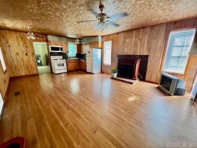 unfurnished living room with plenty of natural light, wooden walls, light wood-type flooring, and a textured ceiling