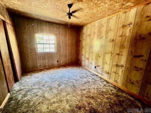 unfurnished room featuring carpet floors, wooden walls, and ceiling fan