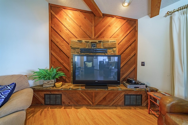 living room featuring wood-type flooring, beamed ceiling, a textured ceiling, and wood walls