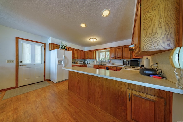 kitchen featuring white appliances, light wood-type flooring, kitchen peninsula, and a textured ceiling