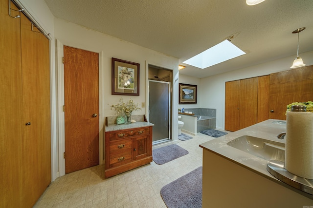 full bathroom featuring a skylight, toilet, shower with separate bathtub, vanity, and a textured ceiling