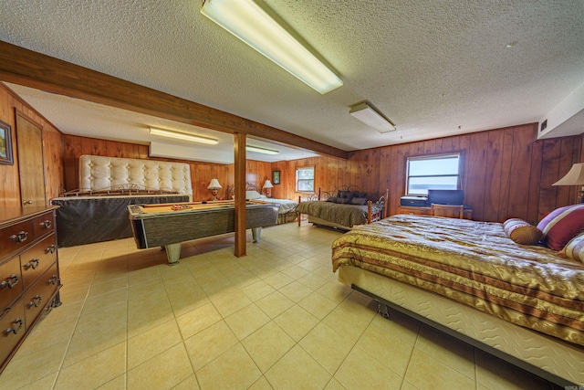 bedroom with beamed ceiling, a textured ceiling, wood walls, and light tile patterned flooring