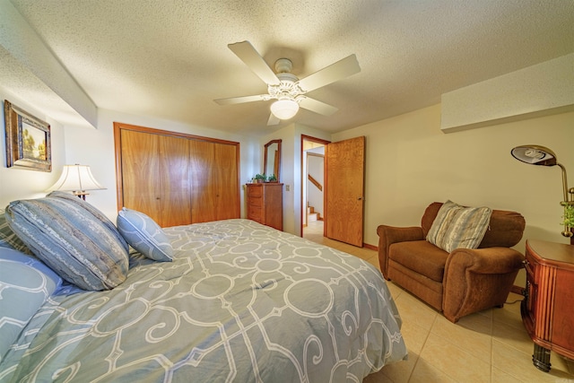 bedroom with ceiling fan, a closet, light tile patterned floors, and a textured ceiling