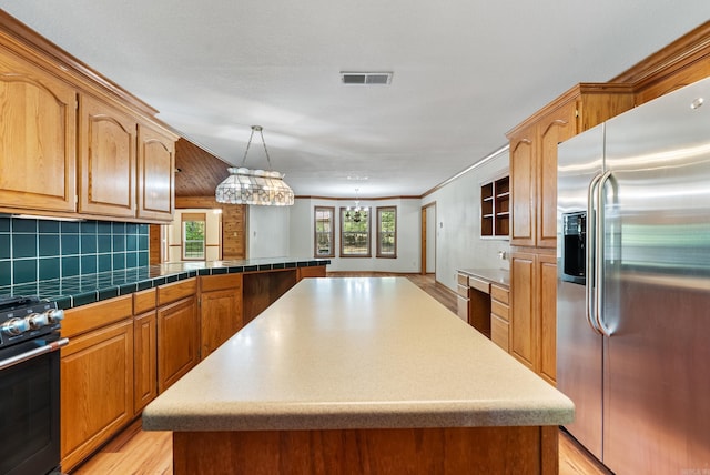 kitchen featuring decorative light fixtures, appliances with stainless steel finishes, light hardwood / wood-style floors, and a center island